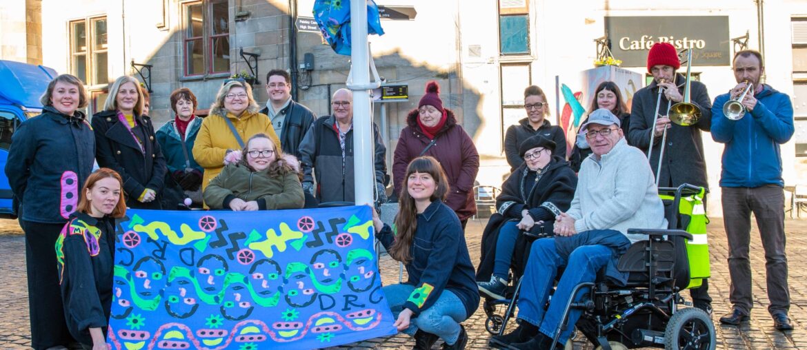 The group from the Disability Resource Centre gathered alongside the artists and musicians from Brass Aye to see the flag raised