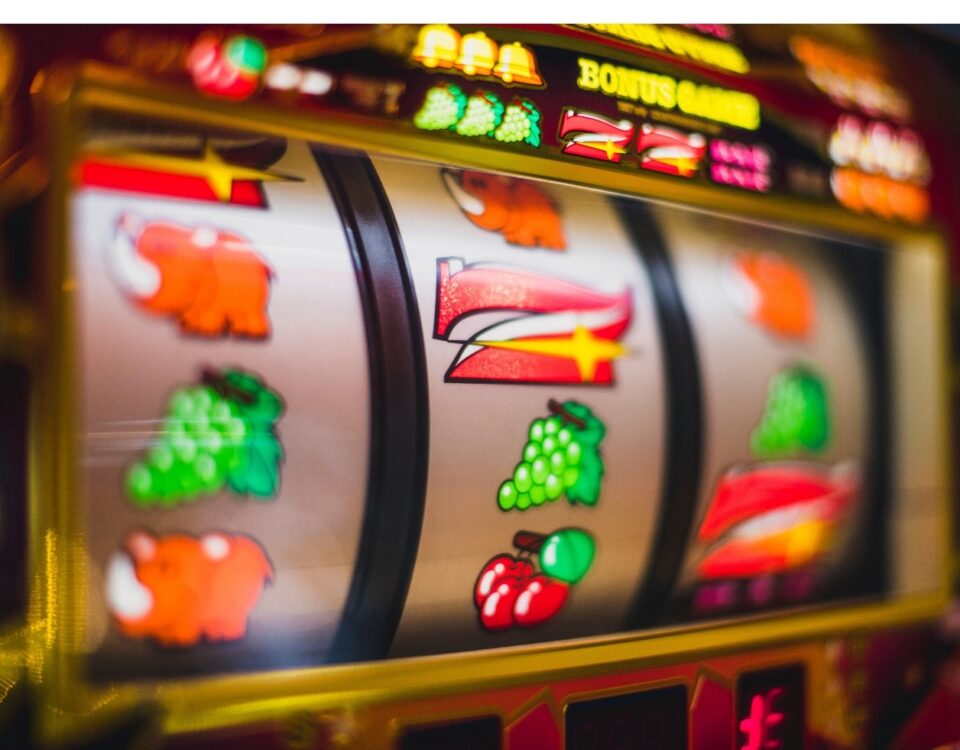 Close-up of a colorful slot machine displaying various fruit symbols like cherries, grapes, and oranges on a spinning reel. Bright lights and a vibrant design enhance the casino theme.