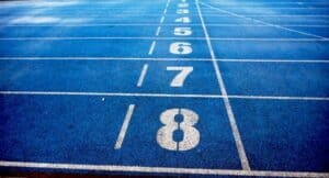 A close-up view of blue running track lanes, numbered 1 to 8 in white, stretching into the distance. Lane numbers are clearly visible and the surface appears slightly wet.