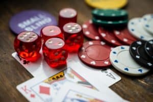 Several red dice, poker chips of various colors, and a King and Ace of hearts playing cards are arranged on a wooden surface, suggesting a gambling or casino theme.