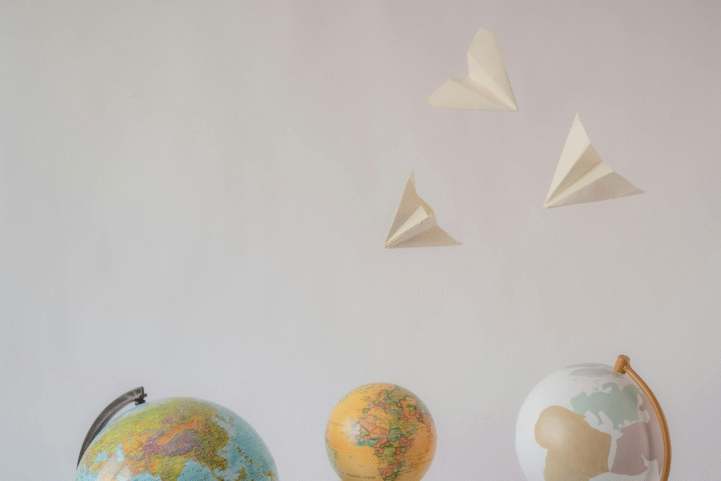 Three globes are lined up at the bottom of the image, and three paper airplanes are flying above them against a plain, light background. The scene suggests themes of travel, exploration, or imagination.
