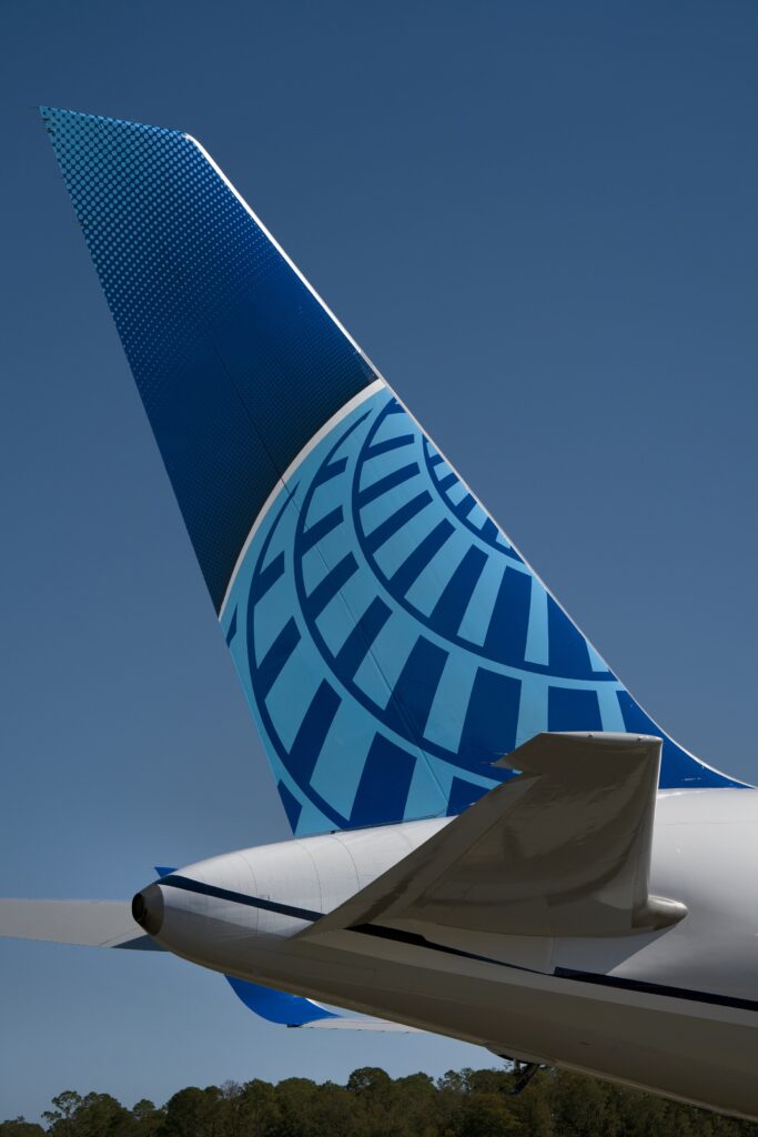 A close-up view of an airplane tailfin featuring a blue geometric circular pattern on a bright blue background, with a clear sky in the background.