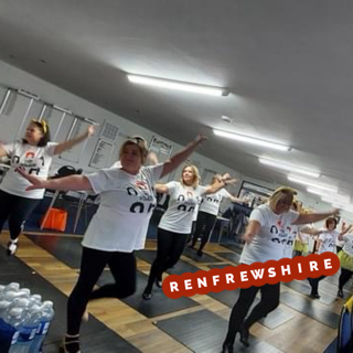 A group of women in matching white t-shirts and black pants dance in a studio with wooden floors. Bottled water is stacked in the foreground. The word "Renfrewshire" appears on the image.