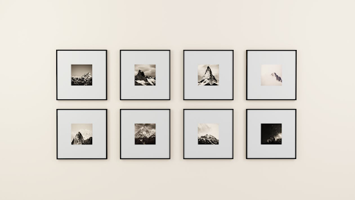 Eight framed black-and-white mountain photographs are arranged in two rows on a plain, light-colored wall. Each frame has a wide white matting, highlighting the small landscape photo in the center.