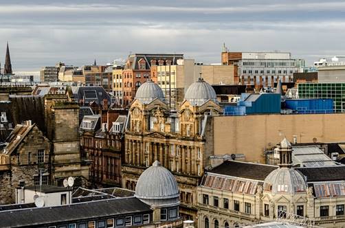 A cityscape with historic buildings featuring domed rooftops in the foreground, surrounded by a mix of older and modern architecture under a cloudy sky.