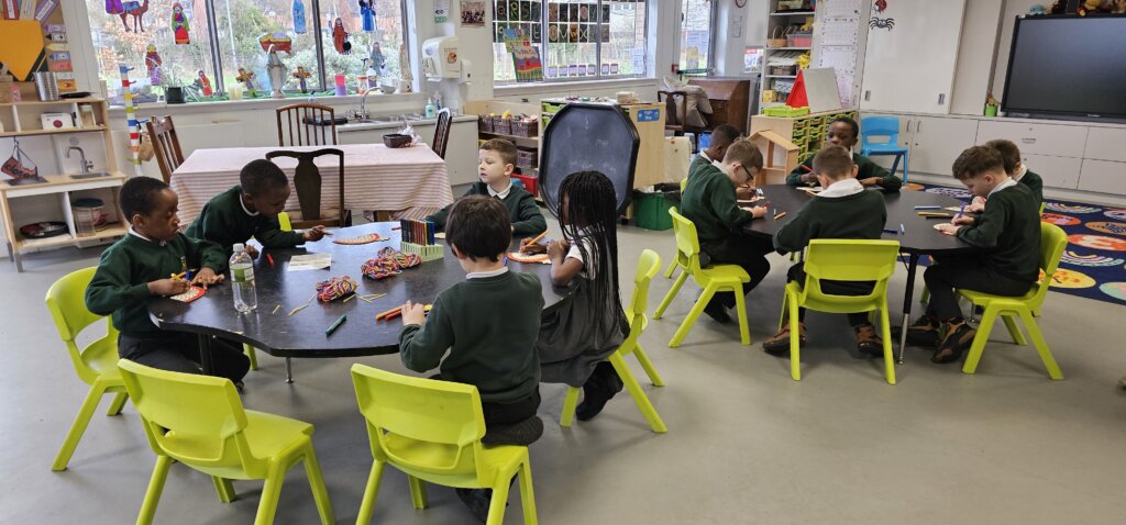 A group of young children sit at two tables in a colorful classroom, engaging in activities with art supplies. The classroom is decorated with artwork, toys, and educational materials.