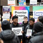A group of young people stand indoors at an event, smiling and holding signs that read "Promise Youthy Fest" and "Promise Human Library." Colorful banners and posters hang behind them.